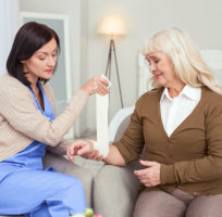 nurse putting bandage at senior woman's wrist